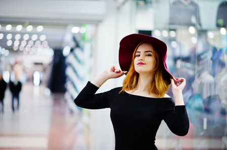 Fashion red haired girl wear on black dress and red hat posed at trade shopping center.の写真素材