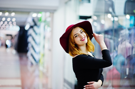 Fashion red haired girl wear on black dress and red hat posed at trade shopping center. Photo toned style Instagram filters.の写真素材