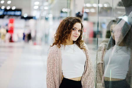Young curly model girl posed on mini skirt at large shopping center near showcase with mannequin.の写真素材