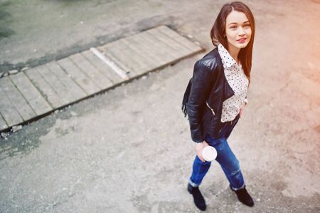 Portrait of stylish young girl wear on leather jacket and ripped jeans with cup of coffee. Street fashion model style.の写真素材