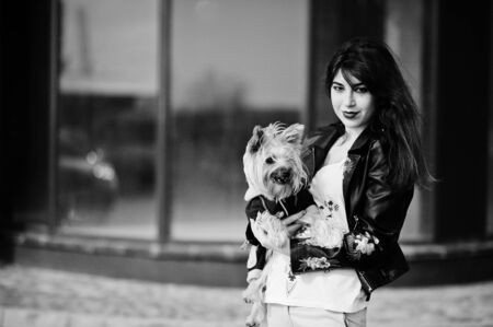 Brunette gypsy girl with yorkshire terrier dog posed against large windows house. Model wear on leather jacket and t-shirt with ornament, pants.の写真素材