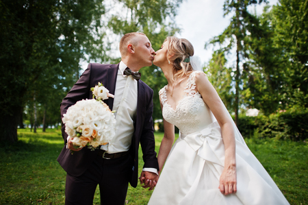 Fashionable kissing wedding couple hugging at green park on sunny wedding day.の写真素材