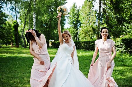 Bride posed on park with two cute brunette bridesmaids on pink dresses.の写真素材