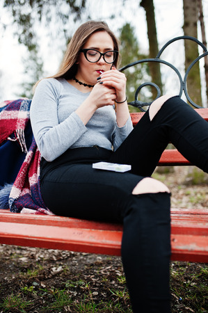Young girl smoking cigarette outdoors sitting on bench. Concept of nicotine addiction by teenagers.の写真素材