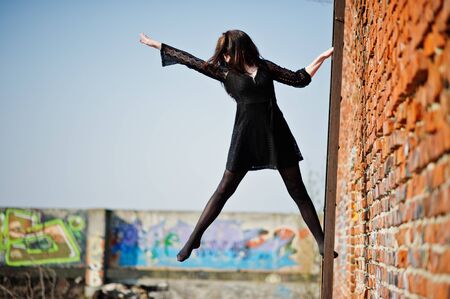 Portrait brunette girl with red lips wearing a black dress posed on the roof at  ladder. Street fashion model.の写真素材
