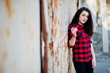 Fashion portrait girl with red lips wearing a red checkered shirt and sunglasses background rusty fence.の写真素材