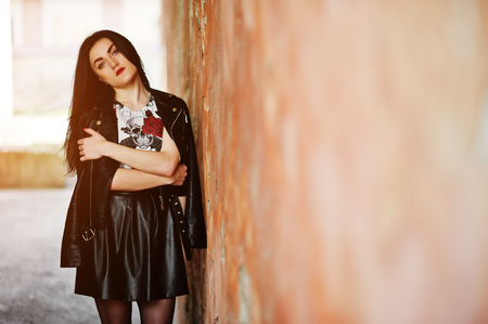 Young goth girl on black leather skirt and jacket against grunge wall.の写真素材