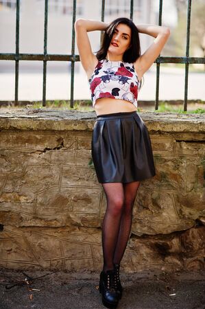 Young goth girl on black leather skirt and high heels punk shoes against iron fence.の写真素材