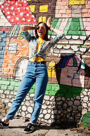 Beautiful fun teenage girl with bananas at hands, wear yellow t-shirt, jeans and sunglasses near graffiti wall.の写真素材