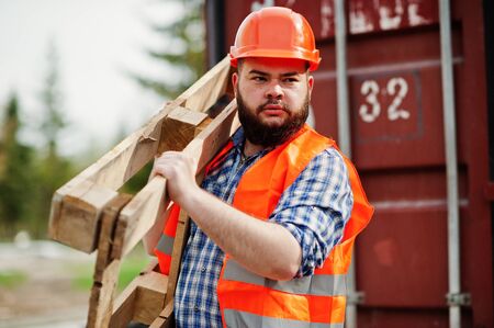 Brutal beard worker man suit construction worker in safety orange helmet with pallet.の写真素材