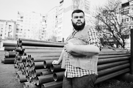 Brutal beard worker man suit construction worker in safety orange helmet near steel pipes.の写真素材