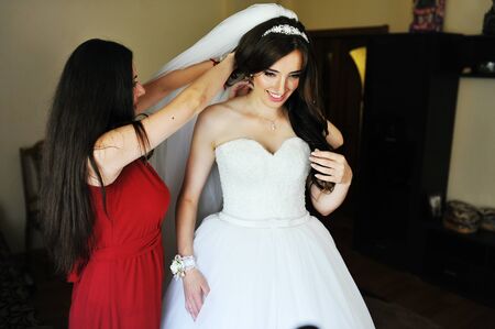 Happy cheerful brunette bride wearing at her room with two bridesmaids on red dress.の写真素材