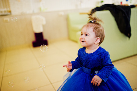 Cute little baby girl at blue dress play with soap bubbles. 1 year birthday day.の写真素材