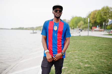 Stylish african american boy wear at cap, football t-shirt and sunglasses. Black sports man portrait.の写真素材