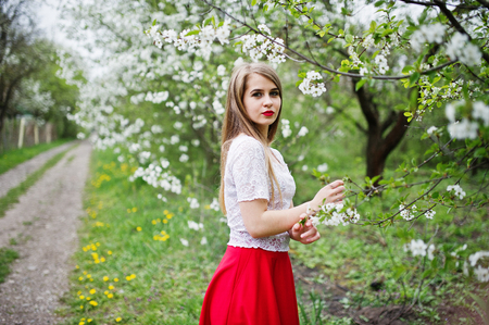 Portrait of beautiful girl with red lips at spring blossom garden, wear on red dress and white blouse.の写真素材