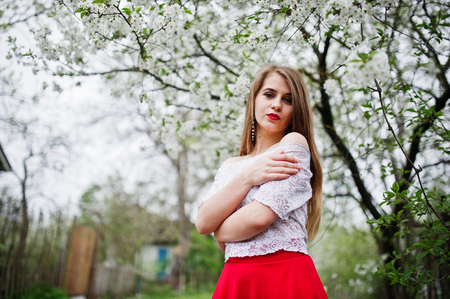 Portrait of beautiful girl with red lips at spring blossom garden, wear on red dress and white blouse.の写真素材
