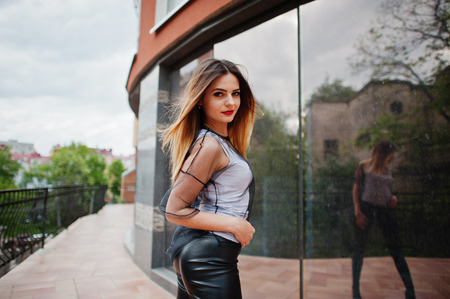 Fashionable woman look at white shirt, black transparent clothes, leather pants, posing at street against large windows of building. Concept of fashion girl.の写真素材