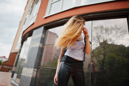 Fashionable woman look at white shirt, black transparent clothes, leather pants, posing at street against large windows of building. Concept of fashion girl.の写真素材