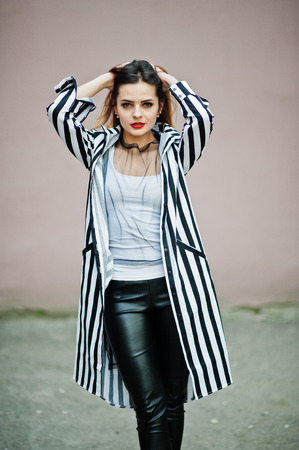 Fashionable woman look with black and white striped suit jacket, leather pants posing against wall. Concept of fashion girl.の写真素材