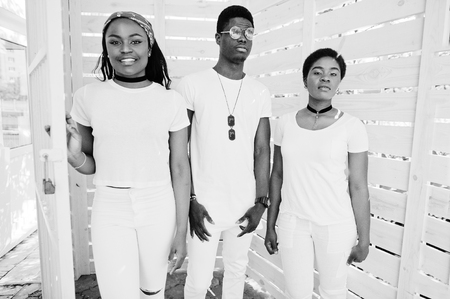 Three stylish african american friends, wear on white clothes against wooden background. Street...