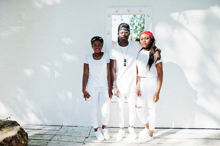 Three stylish african american friends, wear on white clothes against mirror on wall. Street fashion of young black people. Black man with two african girls. の写真素材
