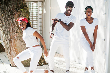 Three stylish african american friends, wear on white clothes. Street fashion of young black people. Black man with two african girls dancing gangsta rap style.の写真素材