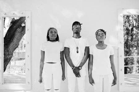 Three stylish and trendy african american friends, wear on white clothes against mirrors. Street fashion of young black people. Black man with two african girls.の写真素材