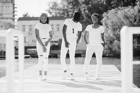 Three stylish african american friends, wear on white clothes. Street fashion of young black people. Black man with two african girls posed.の写真素材