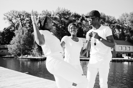 Three stylish, cheerful and trendy african american friends, wear on white clothes. Street fashion of young black people. Black man with two african girls.の写真素材