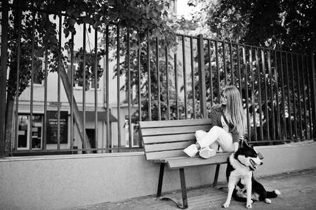 Trendy girl at glasses and ripped jeans with russo-european laika (husky) dog on a leash, against bench on street of city. Friend human with animal theme.の写真素材