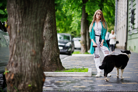 Trendy girl at glasses and ripped jeans with russo-european laika (husky) dog on a leash, against street of city. Friend human with animal theme.の写真素材