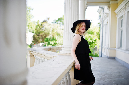 Blonde woman on black dress, necklaces and hat against vintage house.の写真素材