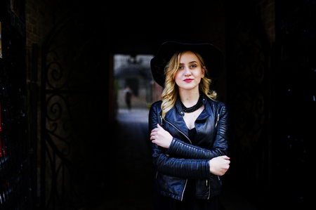 Blonde woman on black dress, leather jacket, necklaces and hat against dark tunnel.の写真素材