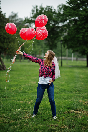 Portrait of brunette girl on checkered shirt, jeans and veil with many red balloons at hen party.の写真素材