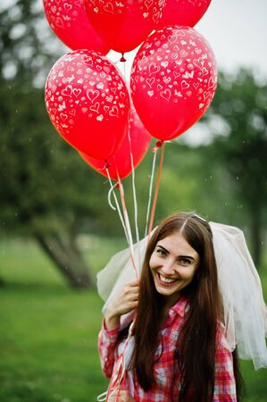 Portrait of brunette girl on checkered shirt, jeans and veil with many red balloons at hen party.の写真素材
