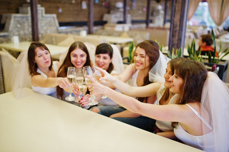 Group of cheerful girls at white shirts sitting at table and drink champagne on hen party.の写真素材