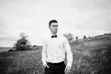 Handsome groom in the middle of the meadow surrounded by tall grass, bushes and rocks.の写真素材