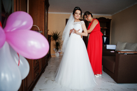 Bridesmaid helping to tie a ribbon on a wedding dress in a room with balloons in it.の写真素材