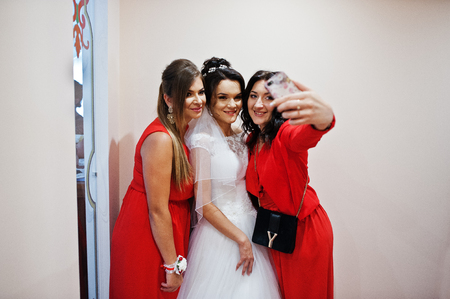 Beautiful bride with cool bridesmaids taking selfie on a smartphone on a wedding day.の写真素材