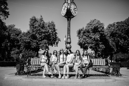Six beautiful young girls sitting on a bench next to the old street clock in the park. Black and white photo.の写真素材