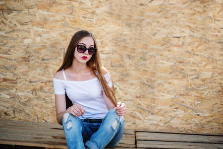 Portrait of a beautiful girl sitting on wooden boards against veneer wall.の写真素材