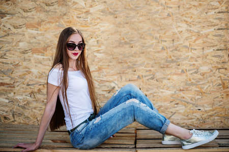 Portrait of a beautiful girl sitting on wooden boards against veneer wall.の写真素材