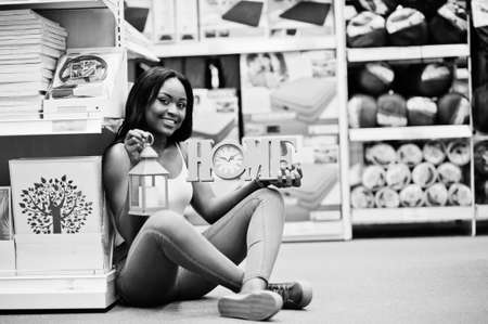Portrait of a beautiful african american woman sitting on the floor with a home sign and a sconce torch in her hands in the store. Black and white photo.の写真素材
