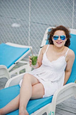 Portrait of an amazing young girl wearing sunglasses enjoying her cocktail sitting on a lounger in lakeside.の写真素材