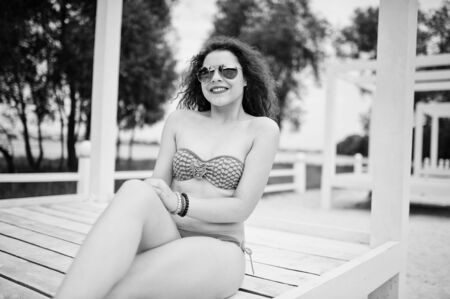 Portrait of an attractive girl posing in bikini with sunglasses on while standing on a white wooden terrace. Black and white photo.の写真素材