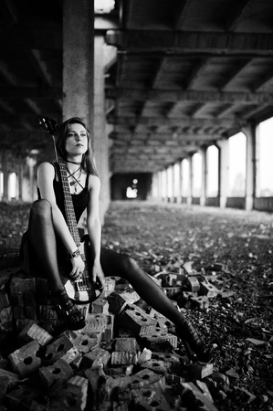 Red haired punk girl wear on black and red skirt, with bass guitar at abadoned place. Portrait of gothic woman musician.の写真素材