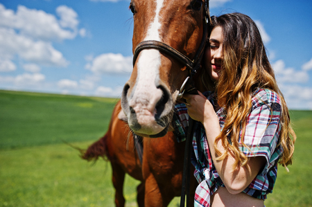 Young pretty girl stay with horse on a field at sunny day.の写真素材