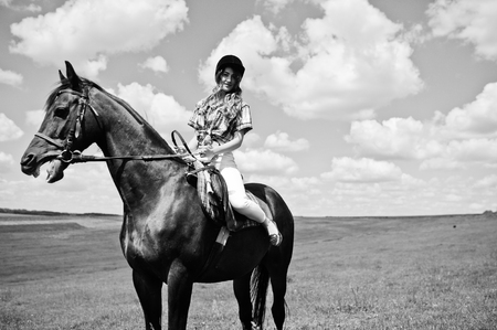 Young pretty girl riding a horse on a field at sunny day.の写真素材