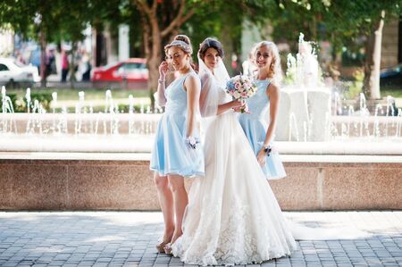 Beautiful bride with bridesmaids posing next to a fountain in the park on a sunny wedding day.の写真素材