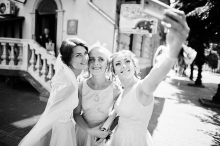 Bride with bridesmaids taking a selfie on city streets. Black and white photo.の写真素材